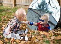 two toddlers playing in the leaves with a mirror behind them and one holding hands