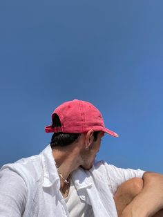 a man wearing a pink hat sitting on top of a wooden bench under a blue sky