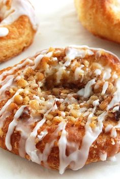 three donuts with icing and nuts on top of white countertop next to other doughnuts