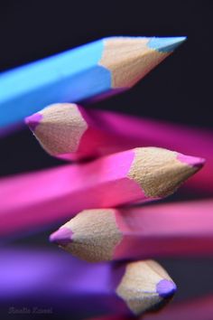 three colored pencils are standing next to each other on a black background with pink, blue, and purple crayons