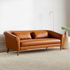 a brown leather couch sitting on top of a carpet next to a vase with a plant