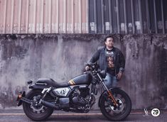 a man standing next to a motorcycle parked on the side of a road in front of a wall