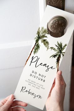 a person holding up a door hanger that says please don't disturb with palm trees on it