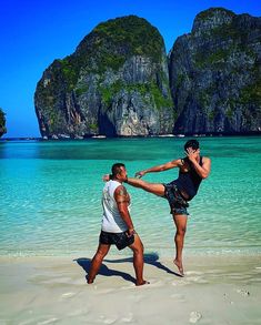 two people on the beach kicking each other in front of some mountains and blue water