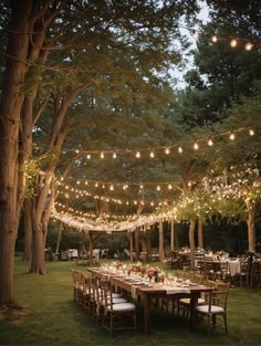 an outdoor dining area with lights strung over the tables and chairs, surrounded by trees