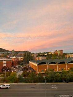 a view of a city from the top of a building at sunset or dawn with cars parked in front of it