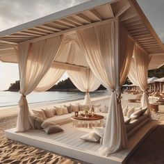 a bed sitting on top of a sandy beach covered in white sheets and drapes