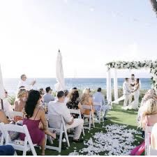 a wedding ceremony on the beach with people sitting in chairs and looking at each other