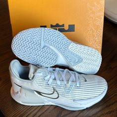 a pair of white nike shoes sitting on top of a wooden table next to an orange box