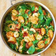 a pan filled with pasta and spinach on top of a wooden table