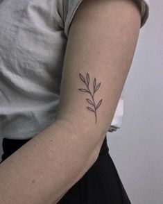 a woman's arm with a small branch tattoo on the left side of her arm