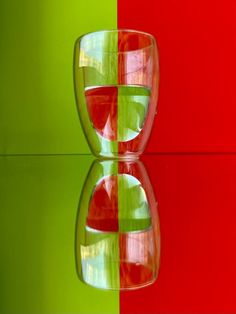 a red and green vase sitting on top of a table next to a glass filled with liquid