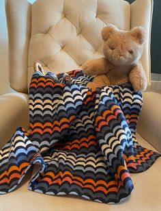 a teddy bear sitting on top of a chair next to a blanket that is folded over it