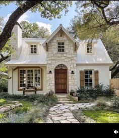 a white house with brown shutters on the front door and windows, surrounded by trees