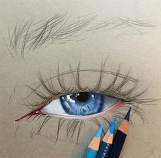 a pencil drawing of an eye with long lashes and blue eyeshade next to two colored pencils