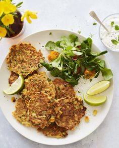 a white plate topped with crab cakes next to a bowl of salad and a cup of yogurt