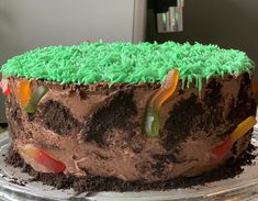 a chocolate cake with green frosting and gummy worms on the top is sitting on a glass platter