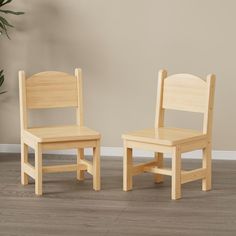 two children's wooden chairs sitting side by side on the floor in front of a plant