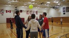 several people standing in a gym with a ball on their head and one person holding the other's hand