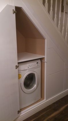 a white washer sitting inside of a dryer in a room under a stair case