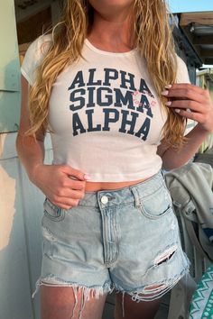 a woman wearing ripped shorts and a white shirt with the words aloha sigma alpha on it