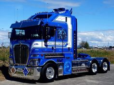 a large blue semi truck parked in a parking lot next to a grass covered field