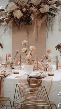 the table is set with pink and white flowers, gold chairs, and greenery