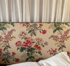 an upholstered headboard with flowers on it in front of a white curtain