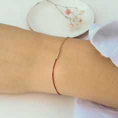 Close-up of hand wearing delicate bracelet of gold chain and red thread with gold beads detail at center. Gold Beaded Chain Friendship Bracelets As Gift, Minimalist Adjustable Chain Bracelet With Tiny Beads, Minimalist Gold Beaded Bracelets For Party, Gold Minimalist Beaded Bracelets For Party, Minimalist Beaded Chain Bracelet, Minimalist Adjustable Chain Bracelet With Gold Beads, Minimalist Adjustable Gold Beads Chain Bracelet, Minimalist Adjustable Gold Beaded Chain Bracelet, Minimalist Gold Beaded Friendship Bracelets