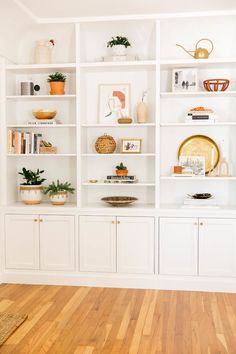 a living room with white bookcases filled with books and vases on top of them