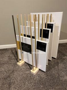 four white and gold bookends with black labels on them in front of a gray wall