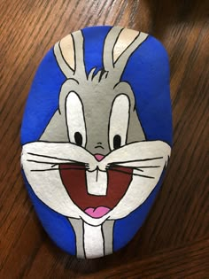 a painted rock with an image of a rabbit's face on it, sitting on a wooden table