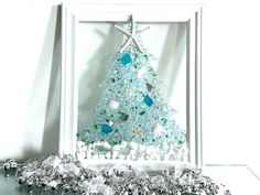 a christmas tree made out of glass beads and other items is displayed in a white frame