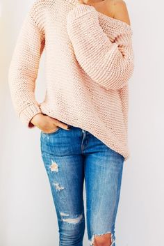 a woman wearing ripped jeans and a pink off the shoulder sweater is standing in front of a white wall