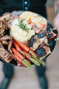 a person holding a plate with meat, vegetables and mashed potatoes on it in their hands