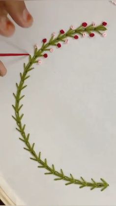 someone is making a wreath with flowers and leaves on the edge of a piece of paper