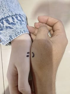 two people holding hands with small tattoos on their fingers and one has a smiley face