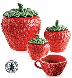 three red ceramic strawberries with green leaves on them, one has a cup and the other has a saucer