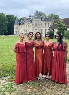 four women in red dresses posing for a photo outside an old building with a castle in the background