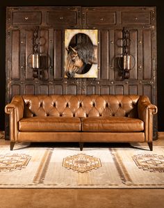 a brown leather couch sitting in front of a wooden paneled wall with a horse painting on it