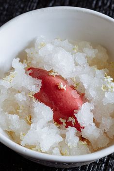 a white bowl filled with sugar and a red piece of food on top of it