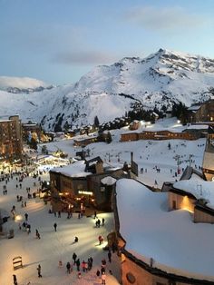 a group of people standing on top of a snow covered slope next to tall buildings