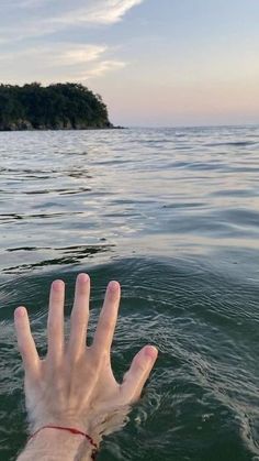 someone's hand in the water with an island in the background