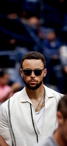 a man wearing sunglasses and a white shirt is standing in front of a crowd at a sporting event