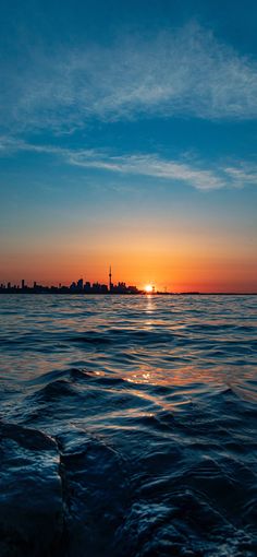 the sun is setting over an ocean with buildings in the distance and blue skies above