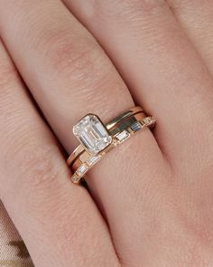 a woman's hand with two gold rings on top of her finger and an engagement ring in the middle