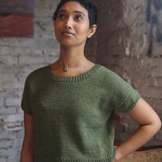 a woman standing in front of a brick wall with her hands on her hips, wearing a green sweater