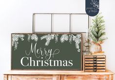 a christmas sign sitting on top of a dresser next to a wooden box with pine branches