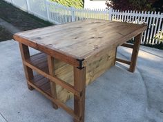 a wooden table sitting on top of a cement ground next to a white picket fence