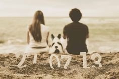 two people sitting on the beach with their dog and new year date written in sand